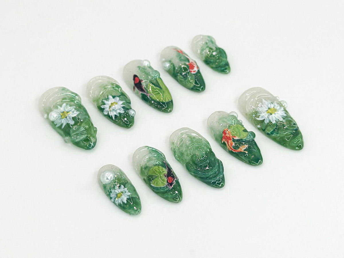Ten green and white nail art designs featuring flowers, leaves, and fish. The designs are painted on clear nail tips.