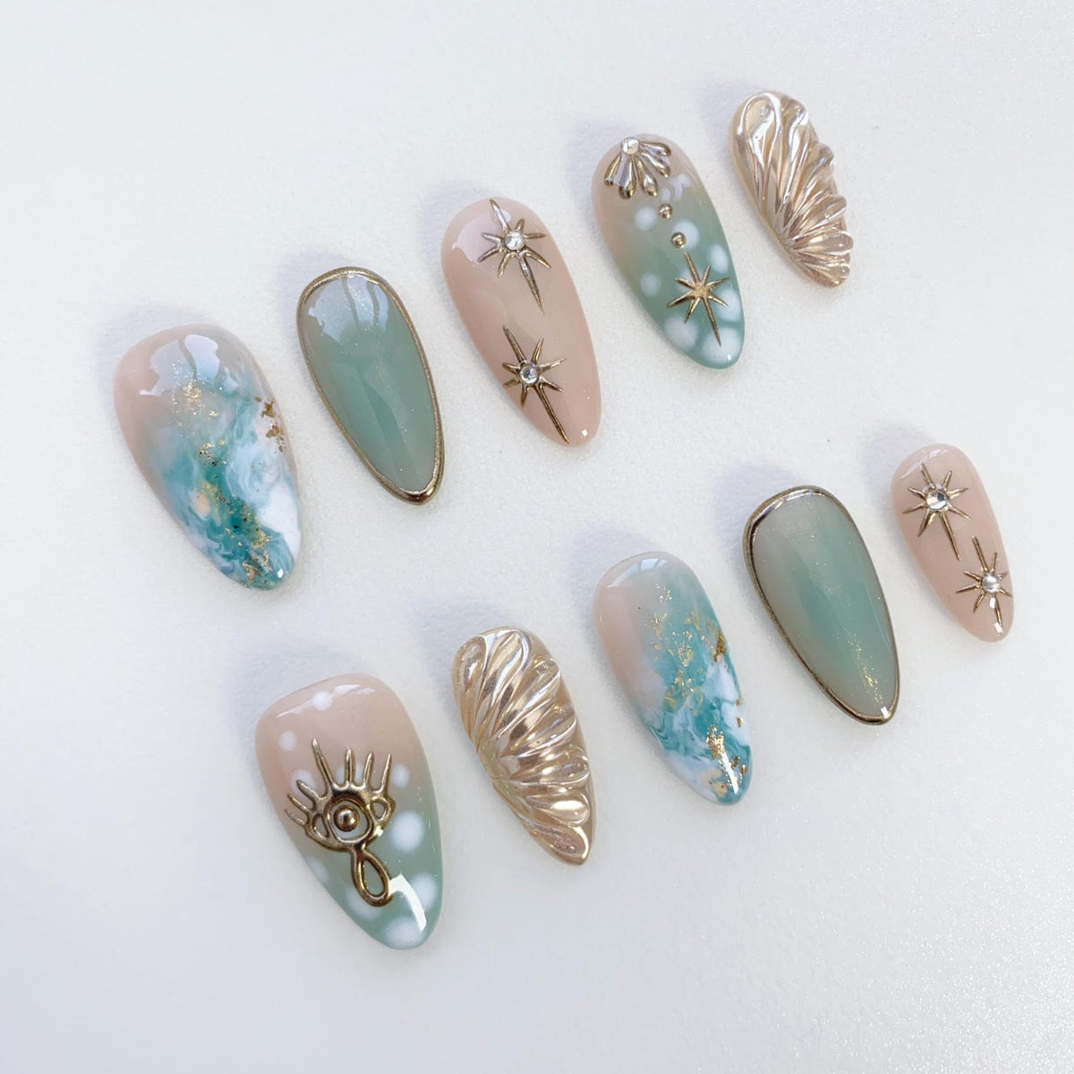 Ten false fingernails with a light pink and blue ombre design. Some nails have gold glitter, gold stars, and gold shell designs.