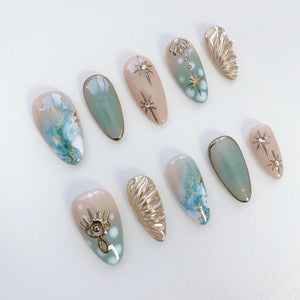 Ten false fingernails with a light pink and blue ombre design. Some nails have gold glitter, gold stars, and gold shell designs.