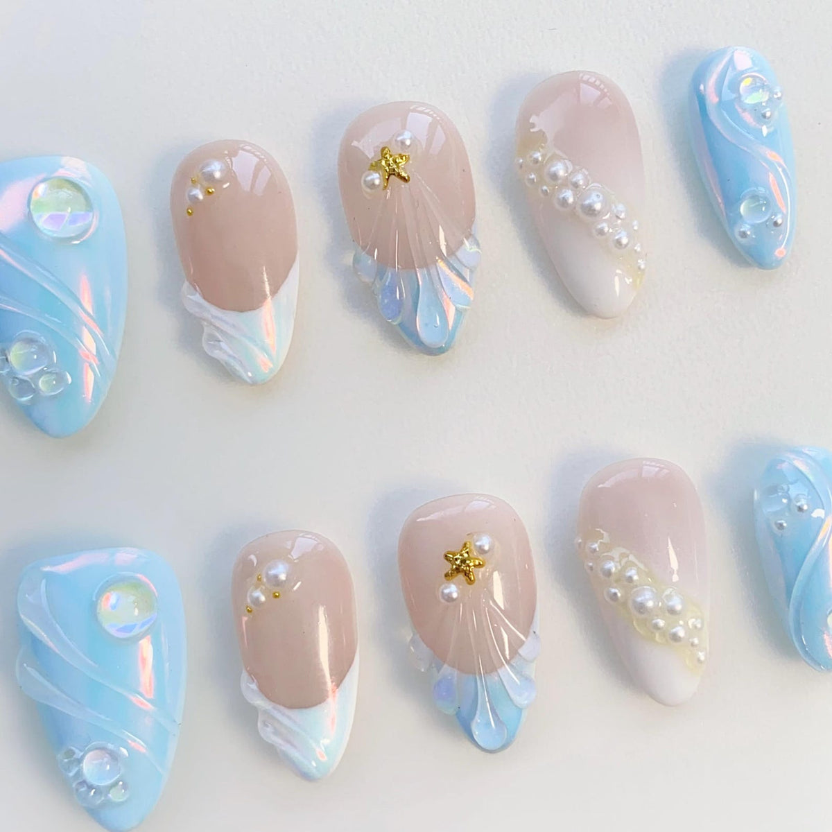 Ten light blue and pink artificial nails with pearl and gold star accents. The nails have a white and light blue design with a pearl and gold star accent.