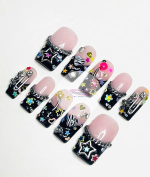 Set of ten black and pink press-on nails with various colorful designs, including stars, hearts, chains, and a safety pin.