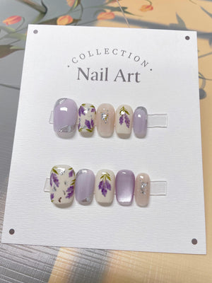 A set of ten lavender-themed nail art tips. The tips are arranged in two rows of five. The tips are decorated with lavender flowers, glitter, and a light purple base.