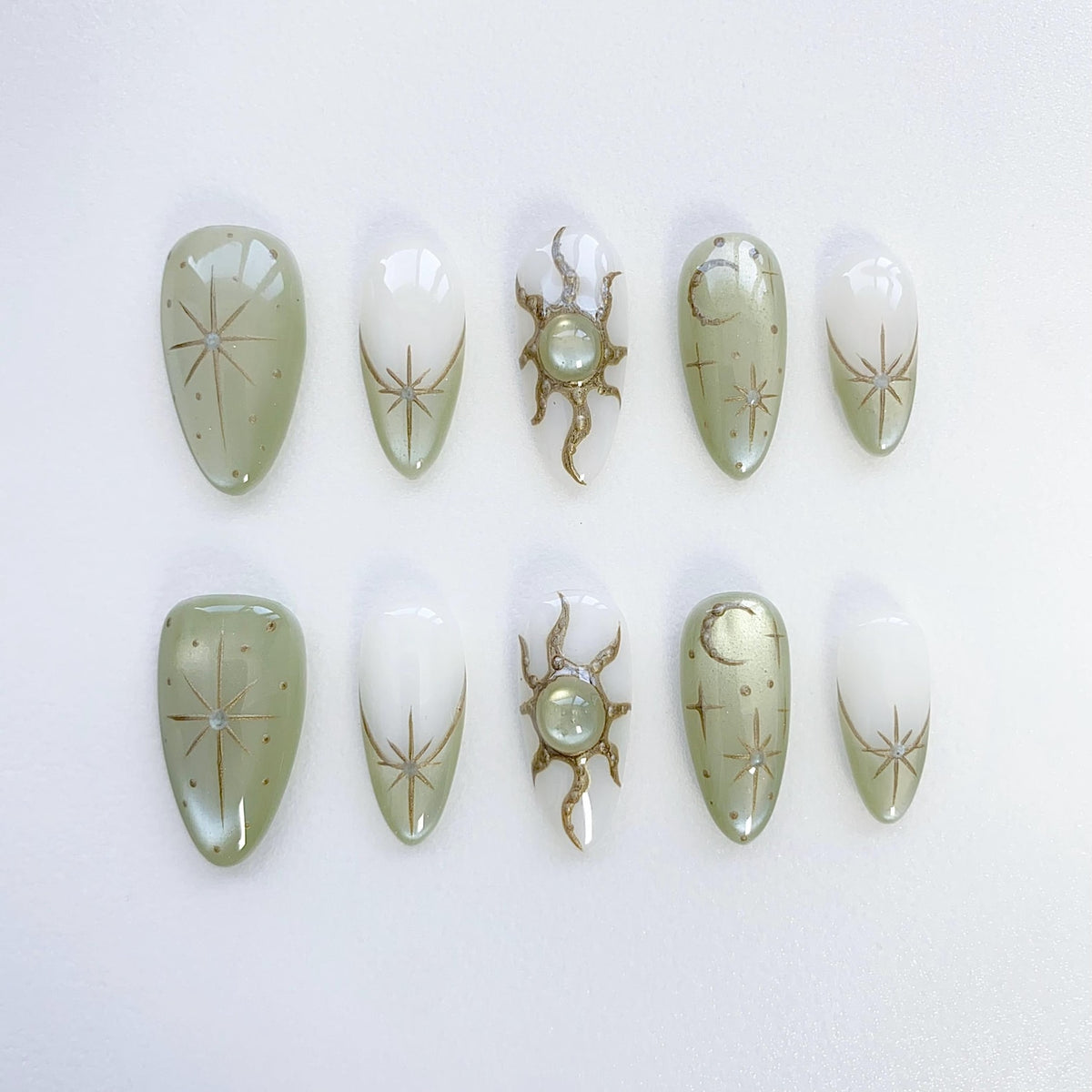 Set of ten green and white oval-shaped press-on nails with gold celestial designs. The designs include stars, moons, and suns.