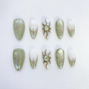 Set of ten green and white oval-shaped press-on nails with gold celestial designs. The designs include stars, moons, and suns.