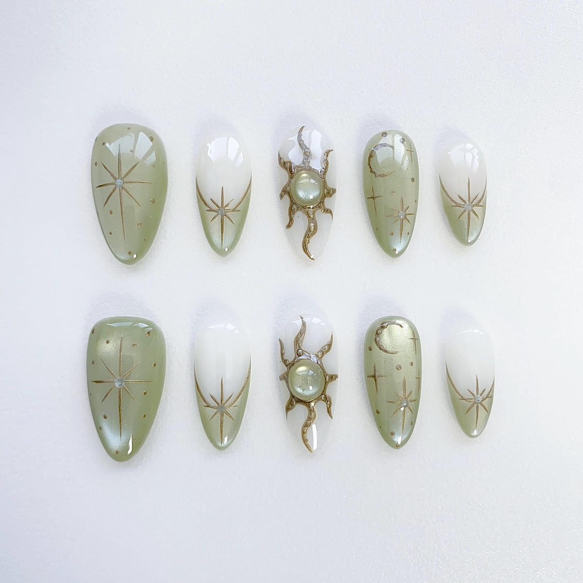 Set of ten green and white false nails with gold celestial designs. The designs include stars, moons, and suns.