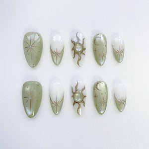 Set of ten green and white false nails with gold celestial designs. The designs include stars, moons, and suns.