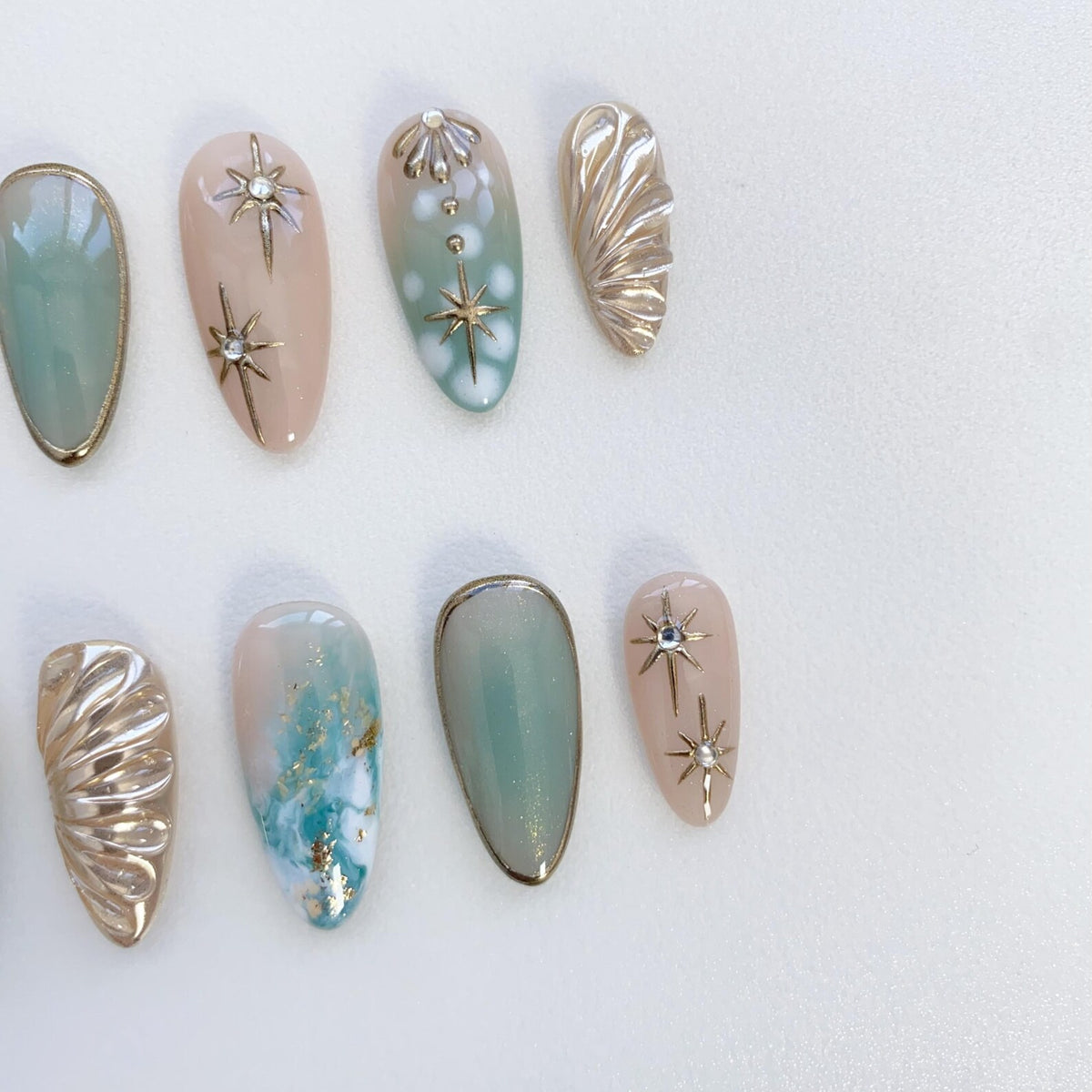 A set of ten false nails with different designs. The nails are in a light pink and light blue color scheme. Some nails have gold stars, others have white flowers, and others have a marble effect.