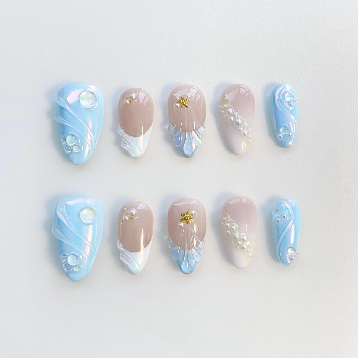 Set of ten false nails with a blue and white pearl design. The nails have a variety of designs, including swirls, pearls, and gold accents.