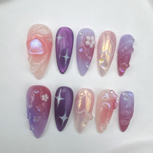 Set of ten false nails with a pink and purple ombre design. Some nails have a heart, flower, or star design.