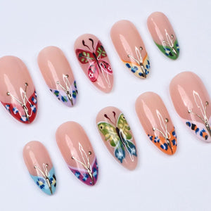 A set of ten artificial nails with a nude base. Each nail features a unique design, including butterfly and floral patterns, and gold-colored accents. The designs incorporate various colors, such as red, green, blue, and orange.