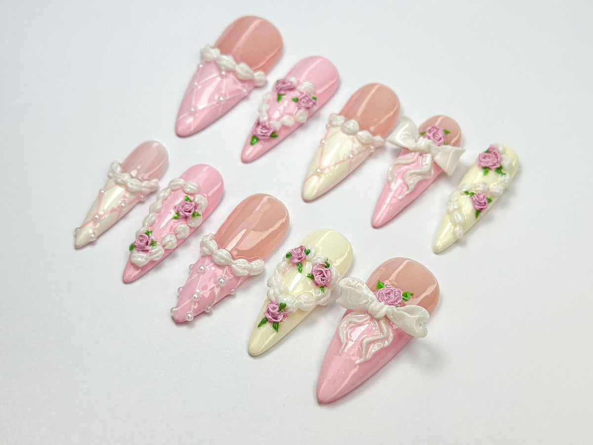 Set of ten pink and white artificial nails with 3D floral designs. Each nail features a different design with pearls, lace, and flowers.
