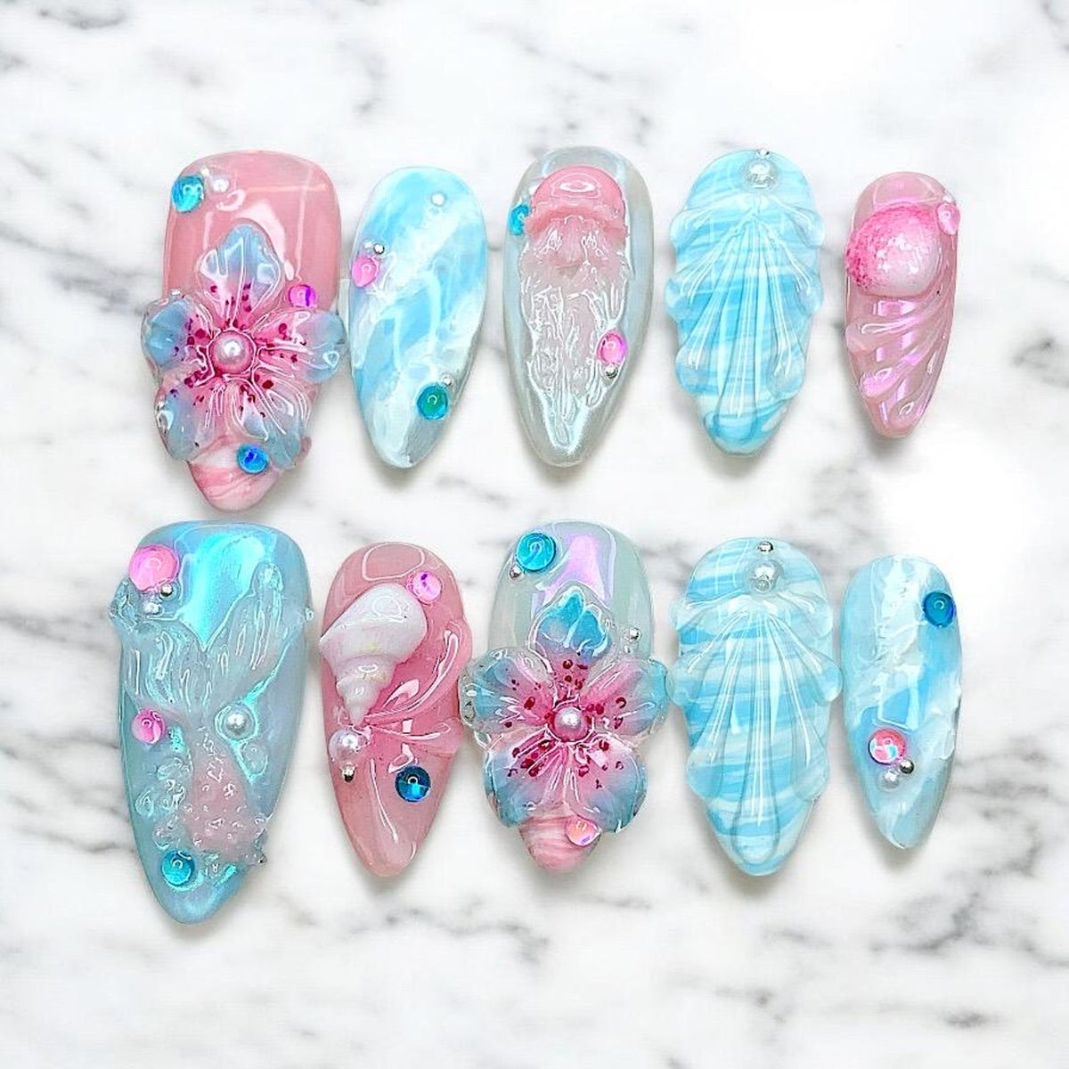 Ten false fingernails with a mermaid theme. The nails are decorated with seashells, flowers, and jellyfish. Some nails are pink and some are blue.