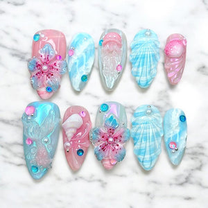 Ten false fingernails with a mermaid theme. The nails are decorated with seashells, flowers, and jellyfish. Some nails are pink and some are blue.