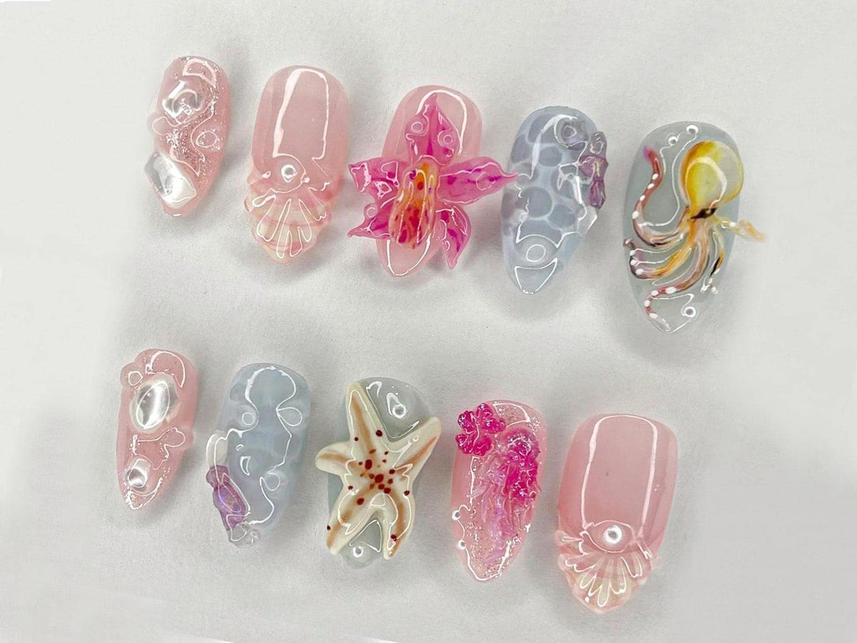 A collection of ten acrylic nails with various designs. The nails feature a range of colors, including pink, blue, and clear, with intricate details such as an octopus, starfish, and floral accents. T