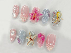 A collection of ten acrylic nails with various designs. The nails feature a range of colors, including pink, blue, and clear, with intricate details such as an octopus, starfish, and floral accents. T