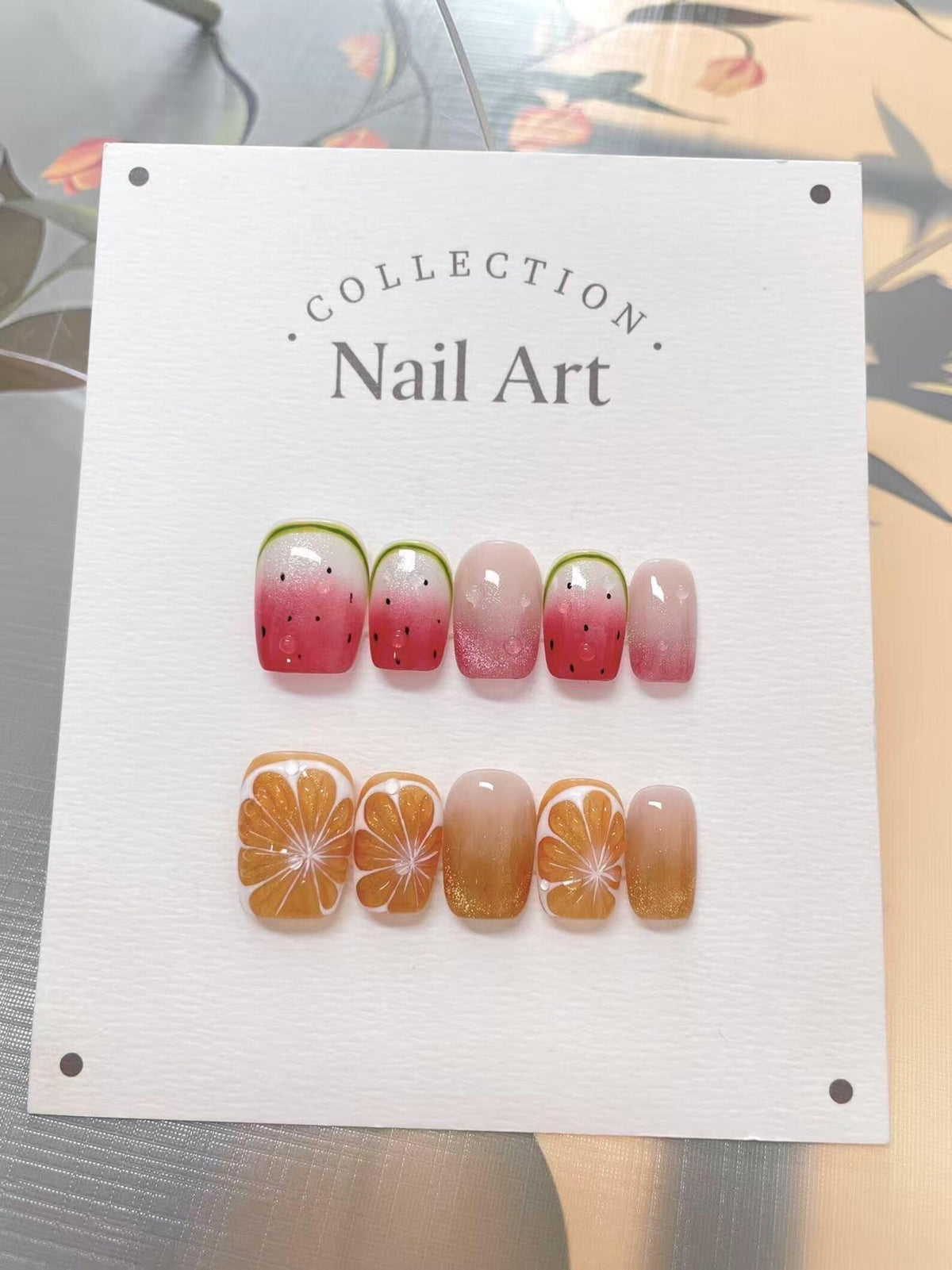A set of press-on nails with fruit designs. The top row features watermelon designs with red, pink, and green accents. The bottom row showcases orange slice designs with gold glitter. The text "Collec