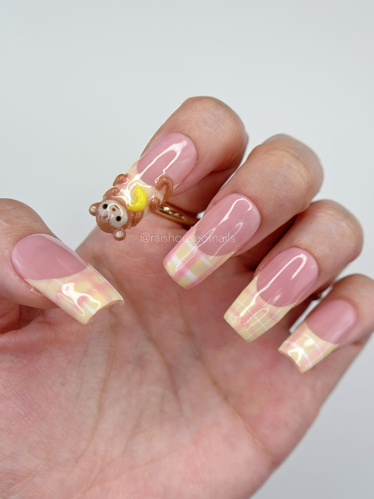 Handmade 3D monkey press on nails with sculpted brown monkey holding a yellow banana and pastel yellow and pink plaid French tips on a pink gel base, shown in square medium by Rai's House of Nails