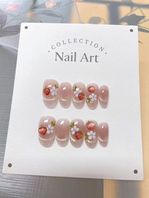 A set of oval-shaped false nails with a light pink base and glitter accents. Each nail features a hand-painted design of a red strawberry and white flowers. The card reads "Collection Nail Art."