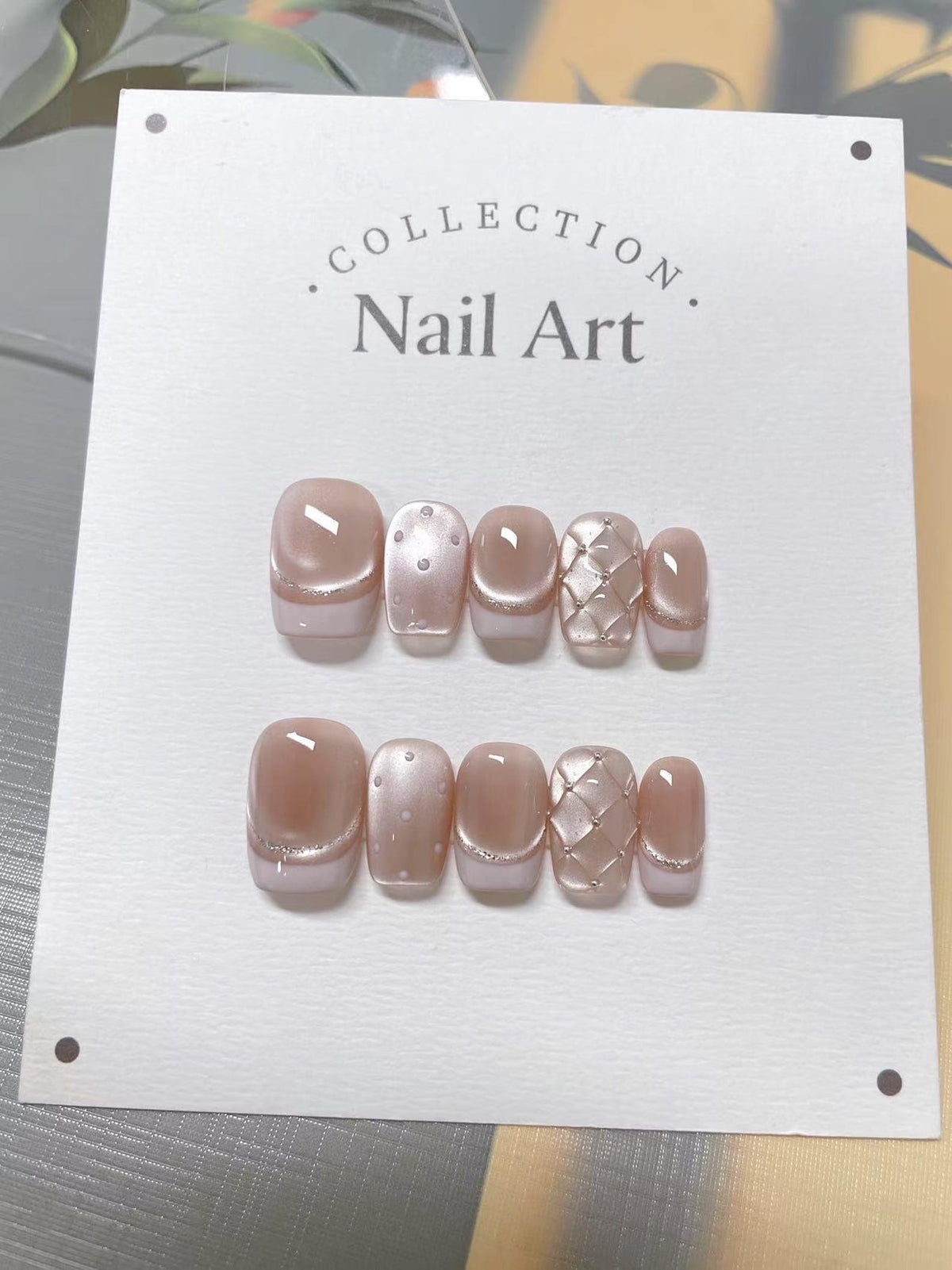A set of press-on nails in a neutral color palette. The nails feature a light pink base with a shimmering accent and decorative patterns. The card reads "COLLECTION. Nail Art."