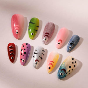 A collection of ten artificial nails, each uniquely designed with a fish theme. The nails feature various colors, including pink, green, silver, and blue, with detailed fish-like patterns and eye acce