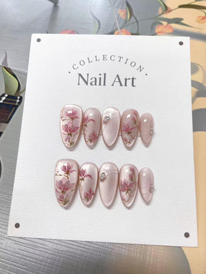 A set of ten almond-shaped press-on nails displayed on a white card labeled COLLECTION Nail Art. The nails feature a pearlescent light pink base with hand-painted pink floral designs, thin silver line