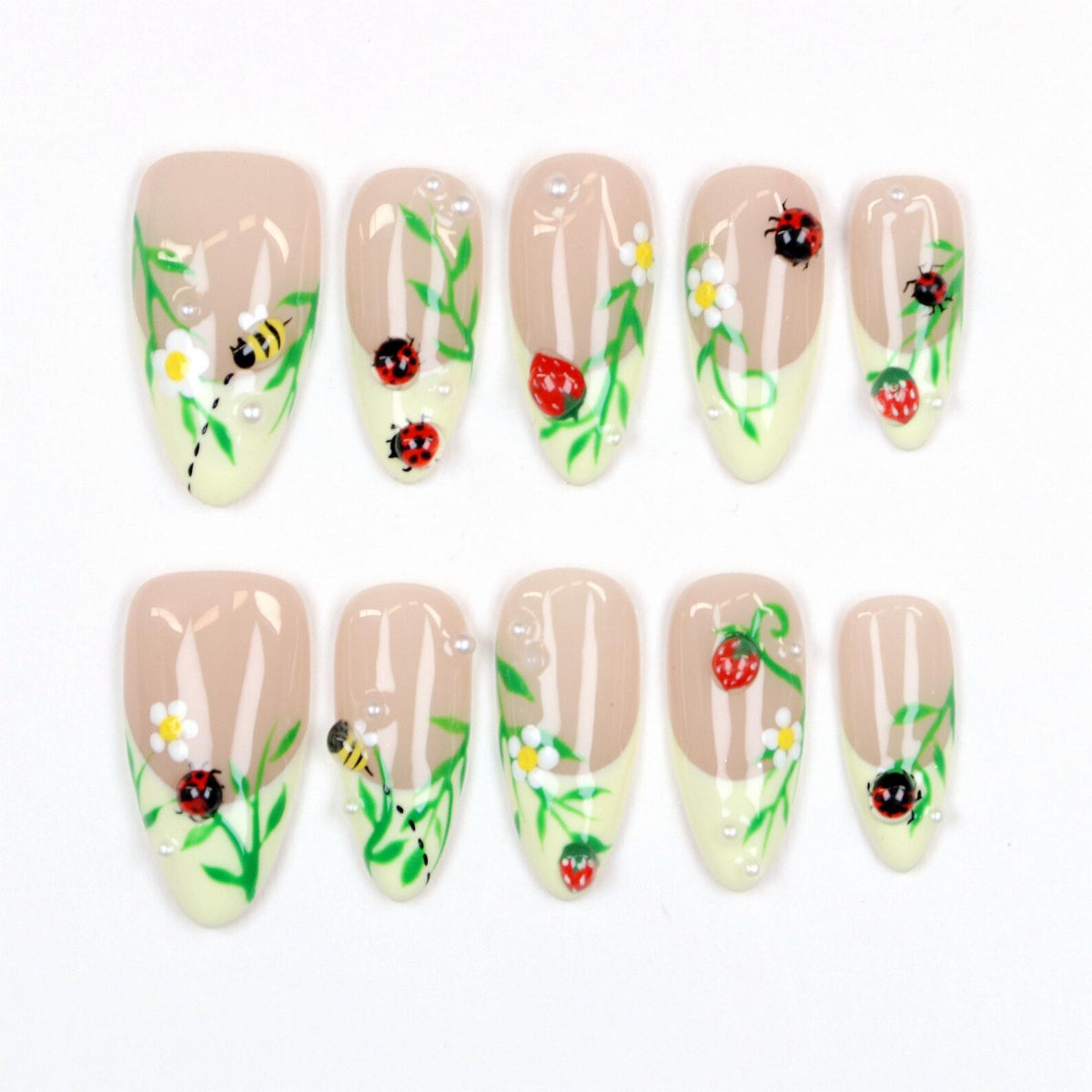 Set of ten almond-shaped false nails. Each nail features a beige base with a light yellow tip. The nails are decorated with green vines, white flowers, red ladybugs, yellow bees, strawberries, and small white pearls.