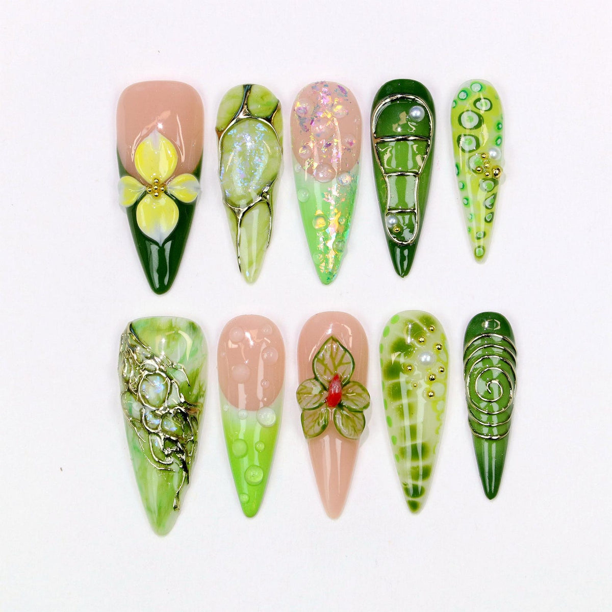 A collection of ten almond-shaped artificial nails with various designs. The nails feature a range of colors, including green, pink, and white, with floral and abstract patterns. Some nails have 3D embellishments and metallic accents.