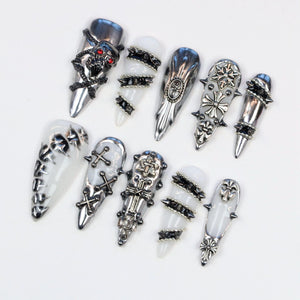 An assortment of silver-toned nail art designs. The collection includes various styles, such as skull, cross, and studded accents. The nails have a glossy finish and are set against a white background, showcasing the intricate details of each design.