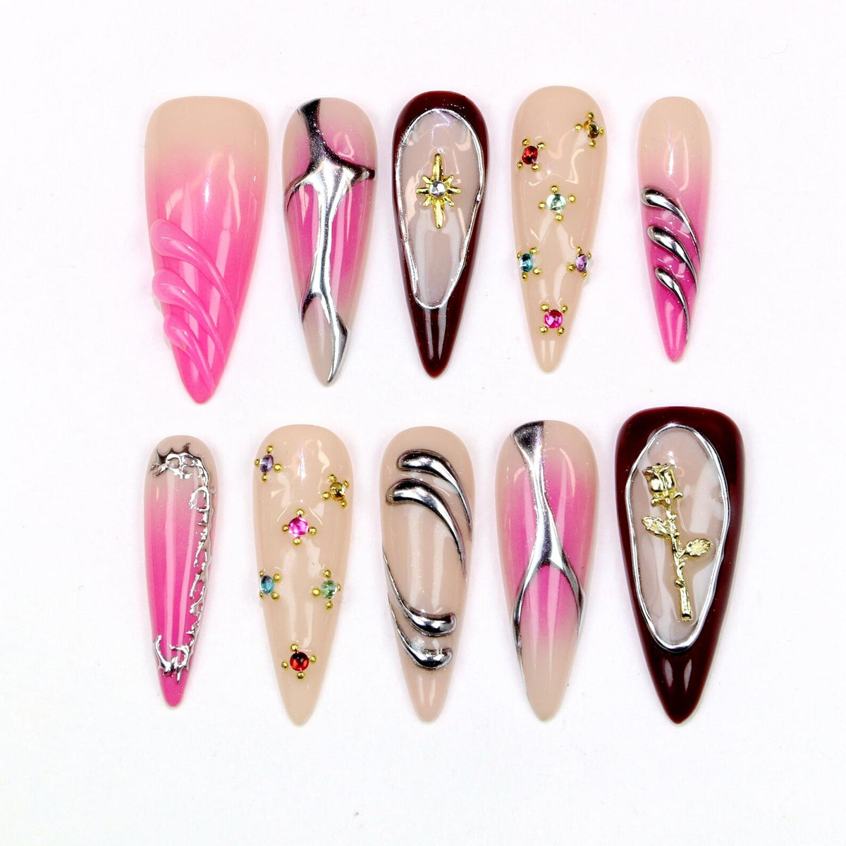 A collection of ten almond-shaped artificial nails. The nails feature various designs, including silver metallic accents, rhinestones, and a gold rose. Colors include pink, nude, and burgundy.