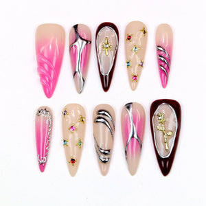 A collection of ten almond-shaped artificial nails. The nails feature various designs, including silver metallic accents, rhinestones, and a gold rose. Colors include pink, nude, and burgundy.