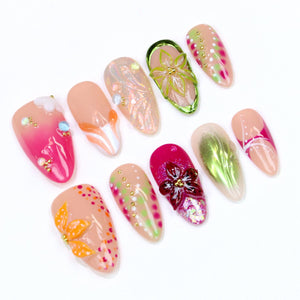 A collection of ten almond-shaped artificial nails with various designs. The nails feature a range of colors, including pink, peach, and green, with floral and abstract patterns. Some nails have 3D embellishments and glitter.