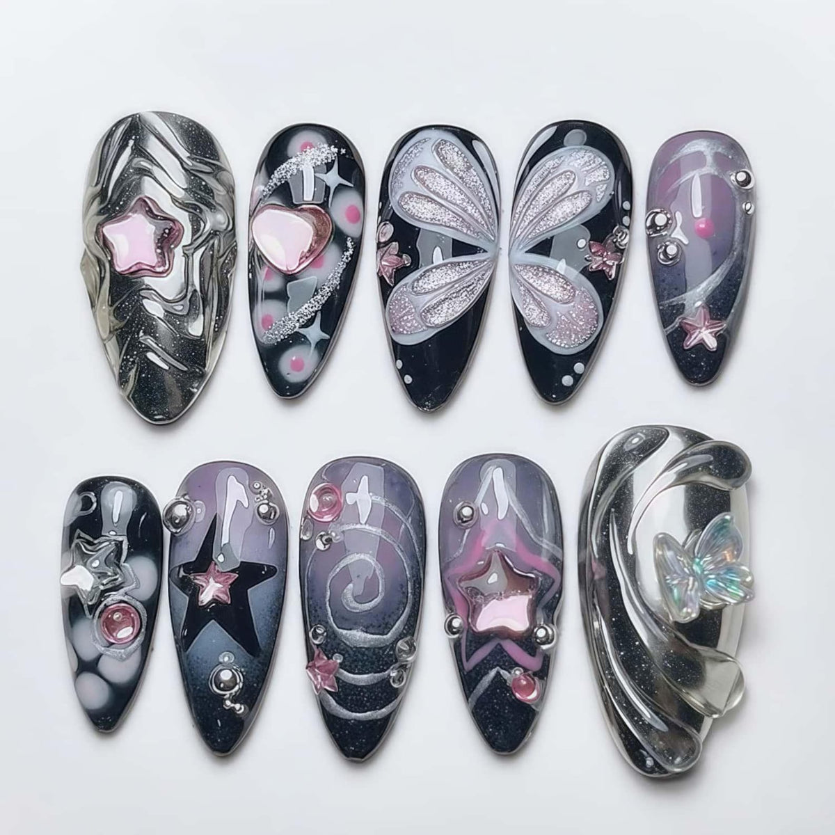 A set of ten almond-shaped artificial nails with various designs. The nails feature silver, black, and purple colors, with star, heart, and butterfly accents. Some nails have 3D embellishments, and others have glitter details.