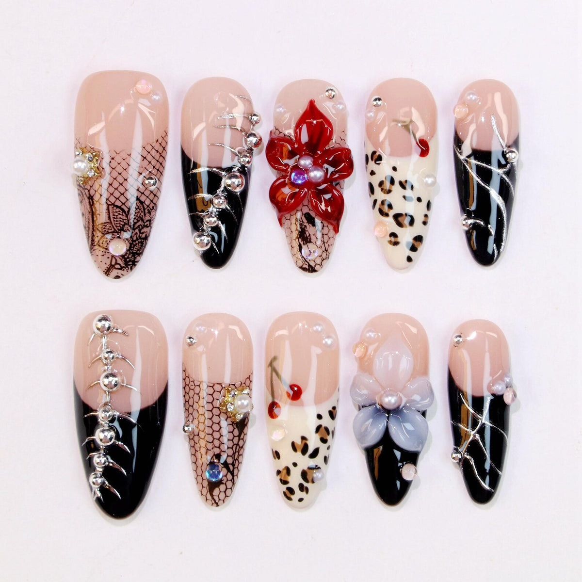 A set of ten artificial nails with various designs. The nails feature a nude base with black, white, and red accents. Some nails have floral, lace, and animal print designs, while others have silver embellishments and pearls.