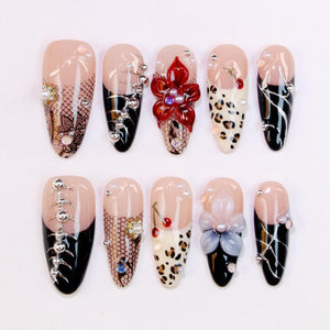 A set of ten artificial nails with various designs. The nails feature a nude base with black, white, and red accents. Some nails have floral, lace, and animal print designs, while others have silver embellishments and pearls.