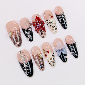 A collection of ten artificial nails with various designs. Some nails feature black and silver accents, while others showcase floral embellishments, leopard print, and lace patterns. Each nail has a nude base with detailed artwork.