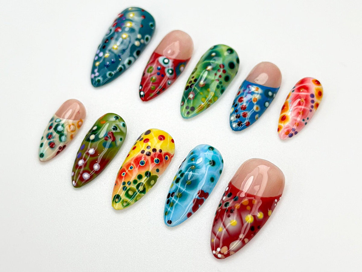 A collection of ten colorful, almond-shaped artificial nails. Each nail features a unique design with a glossy finish, showcasing a variety of colors including teal, red, yellow, green, and blue. The 