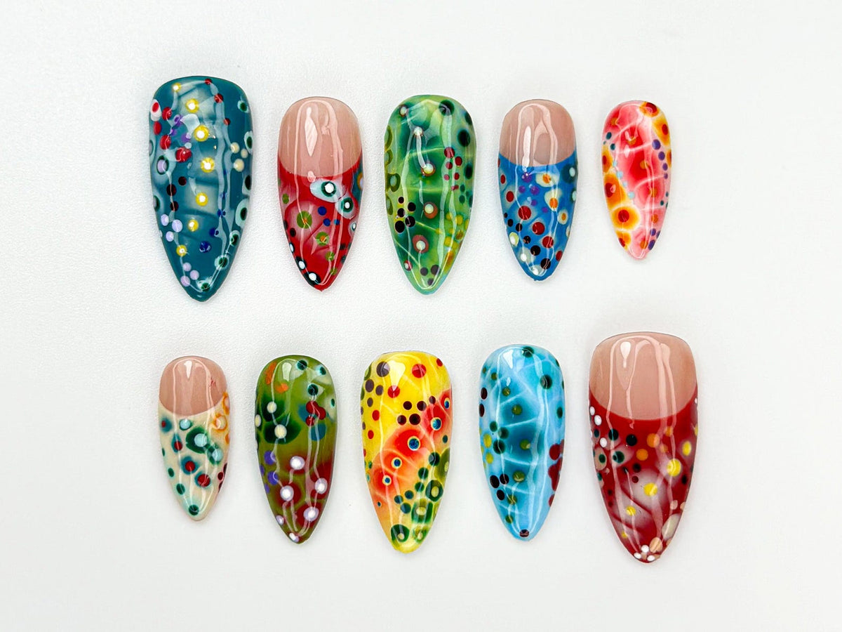 A set of ten colorful, artificial nails with a variety of designs. The nails feature a mix of colors including teal, red, green, yellow, and blue, with dot and swirl patterns. Some nails have a nude-c