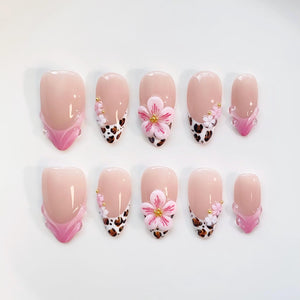A set of ten artificial nails in various sizes. The nails feature a nude base with pink and white accents. Some nails have a leopard print design, while others have 3D pink flower embellishments with gold centers.