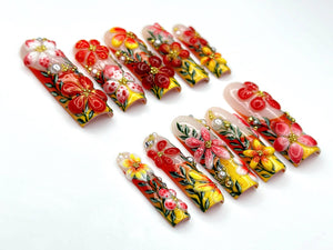 A set of press-on nails with a floral design. The nails feature a variety of colors, including red, yellow, and white, with intricate details. Some nails have small, decorative gems.