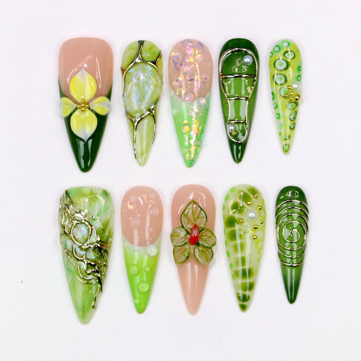 A collection of ten artificial nails with various designs. The nails feature a range of colors, including green, pink, and gold, with floral and abstract patterns. Some nails have 3D embellishments, while others have glitter and pearl accents.