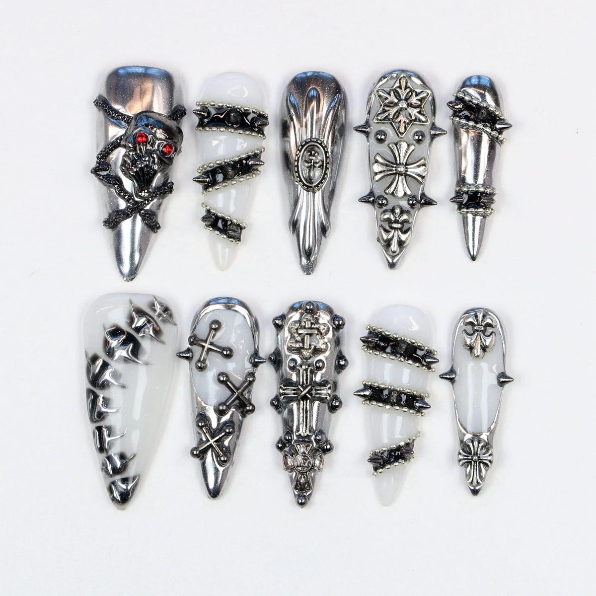 A collection of ten silver-colored, gothic-style nail art designs. Each nail features unique embellishments, including skulls, crosses, spikes, and geometric patterns. The nails are displayed against a white background.