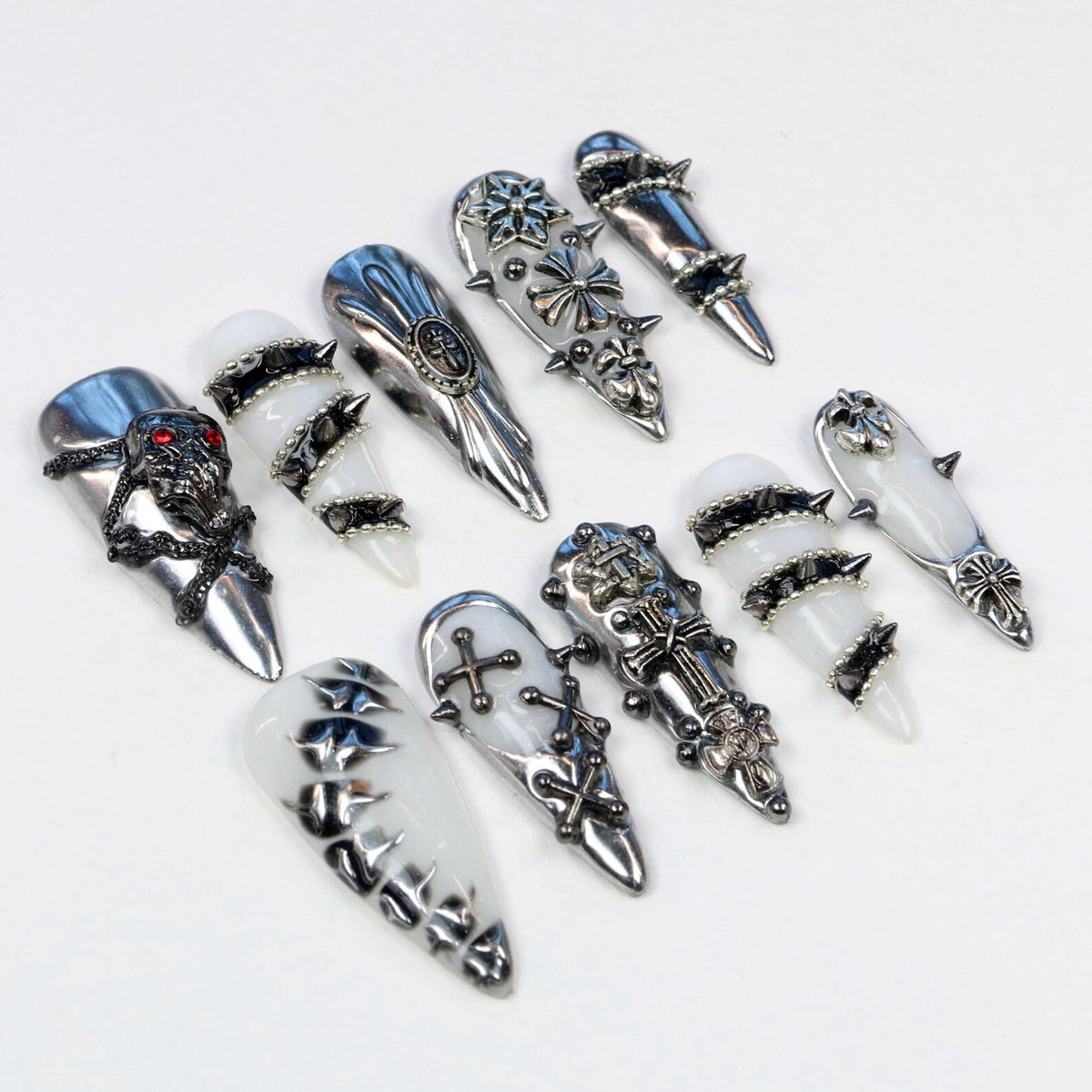 An assortment of silver-toned nail armor, featuring various designs. Some pieces have skull, cross, and floral motifs, while others have a smooth, polished finish. The nail armor is displayed against a white background.