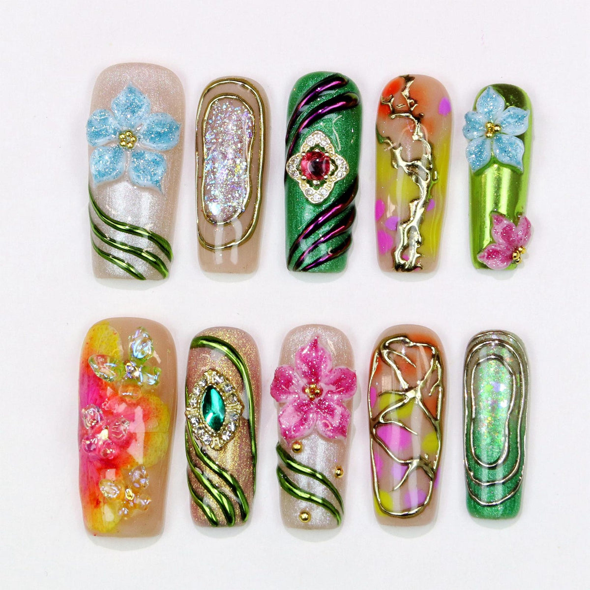 A collection of ten artificial nails with various designs. The nails feature a range of colors, including green, pink, gold, and blue, with embellishments such as flowers, glitter, and gemstones. The designs are intricate and artistic, showcasing nai