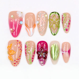 A collection of ten almond-shaped artificial nails with various designs. The nails feature a range of colors, including pink, orange, green, and nude, with embellishments like flowers, dots, and glitter. Some nails have a glossy finish, while others 