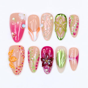 A collection of ten artificial nails in various designs. The nails feature a range of colors, including pink, orange, green, and beige, with floral and abstract embellishments. Some nails have 3D elements and glitter.