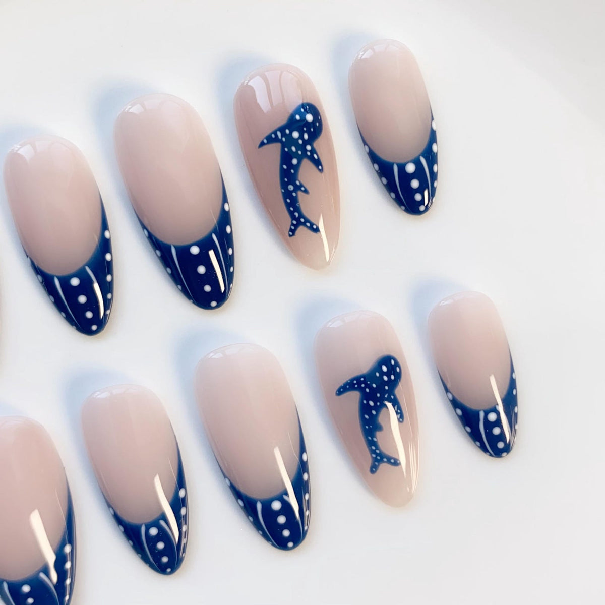 Oval-shaped artificial nails with a light pink base and a dark blue French tip with white polka dots. Some nails feature a dark blue whale shark design.