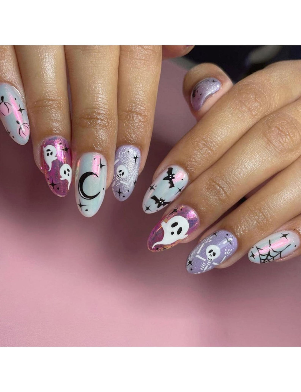 Oval-shaped nail art featuring Halloween-themed designs. The nails showcase ghosts, bats, spiderwebs, and skeletons in white and black against a backdrop of pink, purple, and silver glitter. The designs are applied on a light pink background.