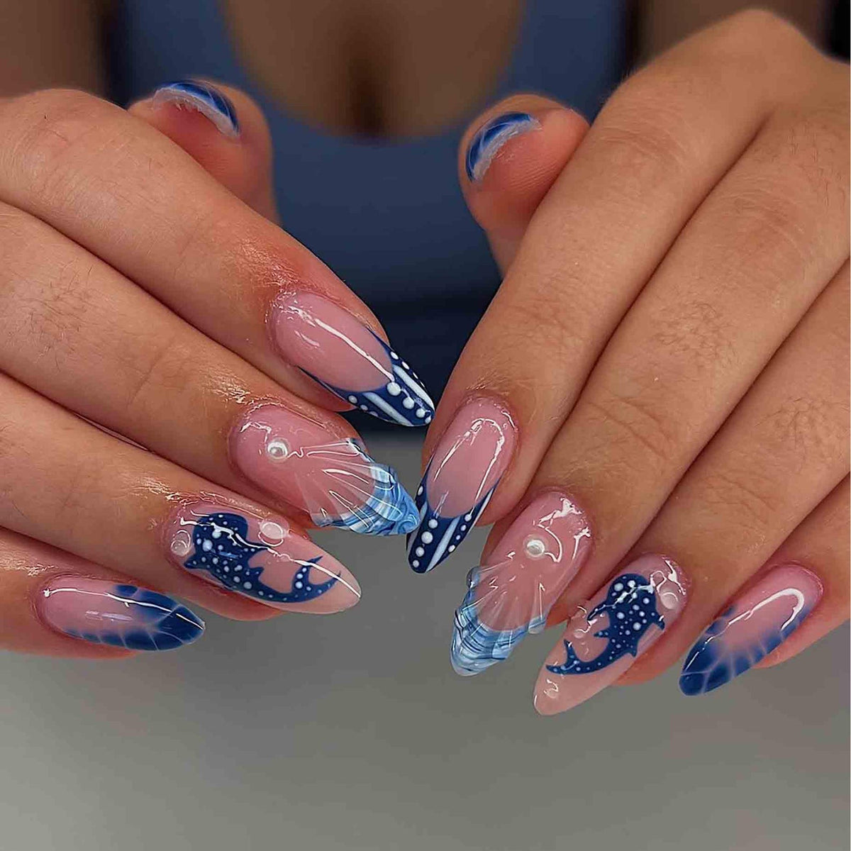 Long, almond-shaped acrylic nails with a clear base and a French tip design. The tips feature a navy blue and white pattern, with a whale design on some nails. Some nails have a pearl accent.