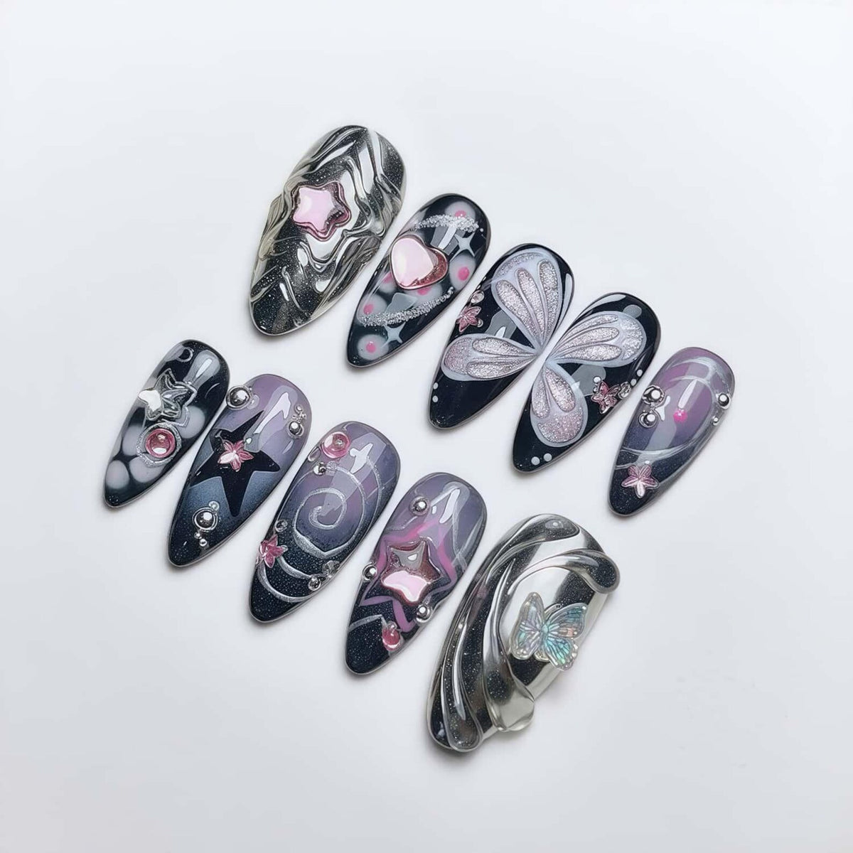 A collection of long, almond-shaped artificial nails with various designs. The nails feature patterns like swirls, stars, hearts, and butterfly wings, in colors including silver, black, pink, and purple. Some nails have small, decorative embellishmen