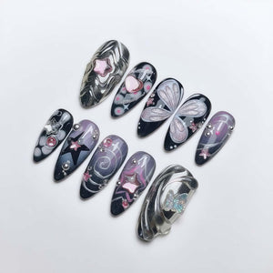 A collection of long, almond-shaped artificial nails with various designs. The nails feature patterns like swirls, stars, hearts, and butterfly wings, in colors including silver, black, pink, and purple. Some nails have small, decorative embellishmen